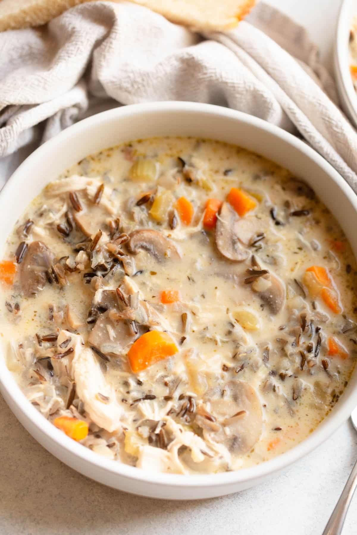 Crockpot Chicken and Mushroom Wild Rice Soup in a white bowl wiht a cream colored napkin next to it. 