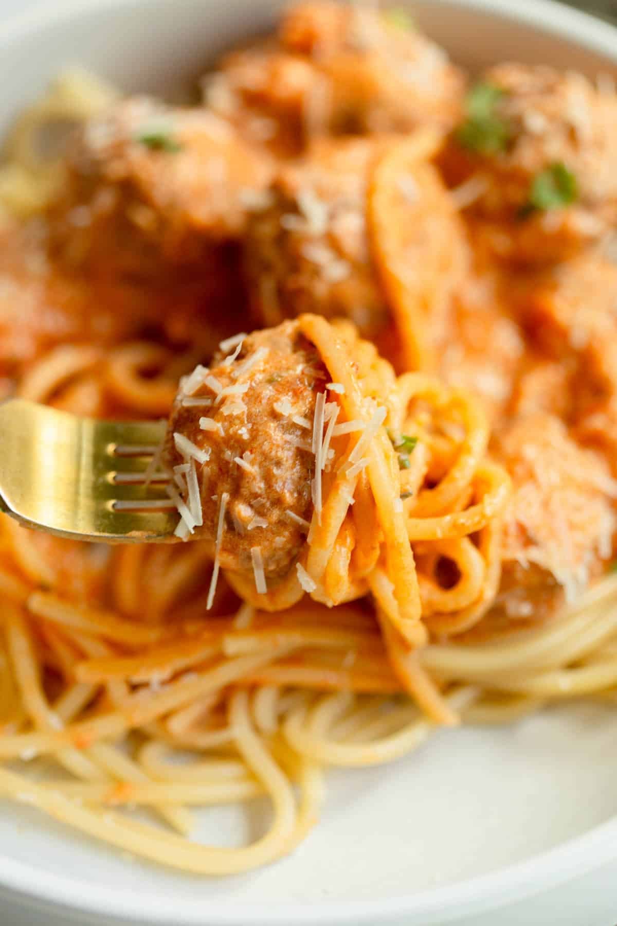 Crockpot Marinara Alfredo Meatball with spaghetti noodles on a gold fork.