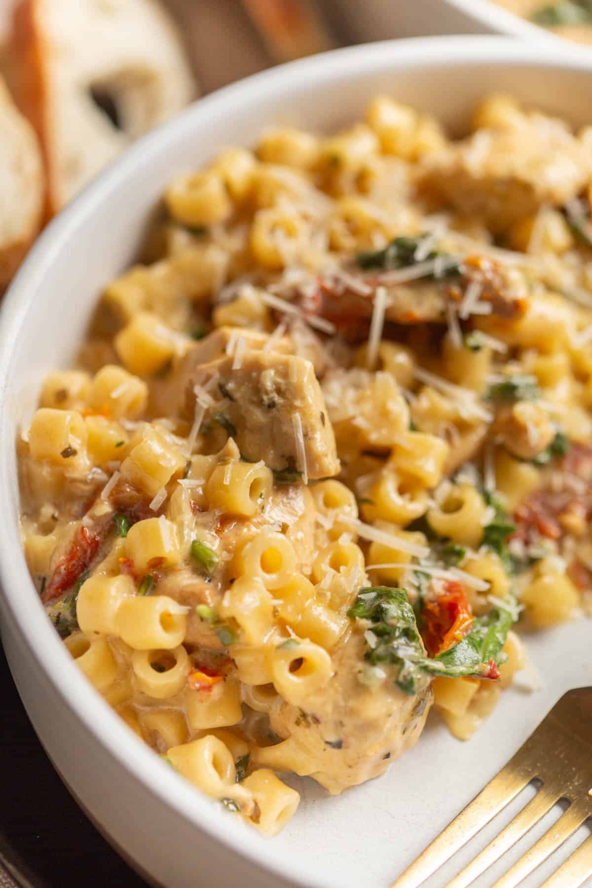 Crockpot Marry Me Chicken Pasta in a shallow cream bowl with a gold fork in it. 