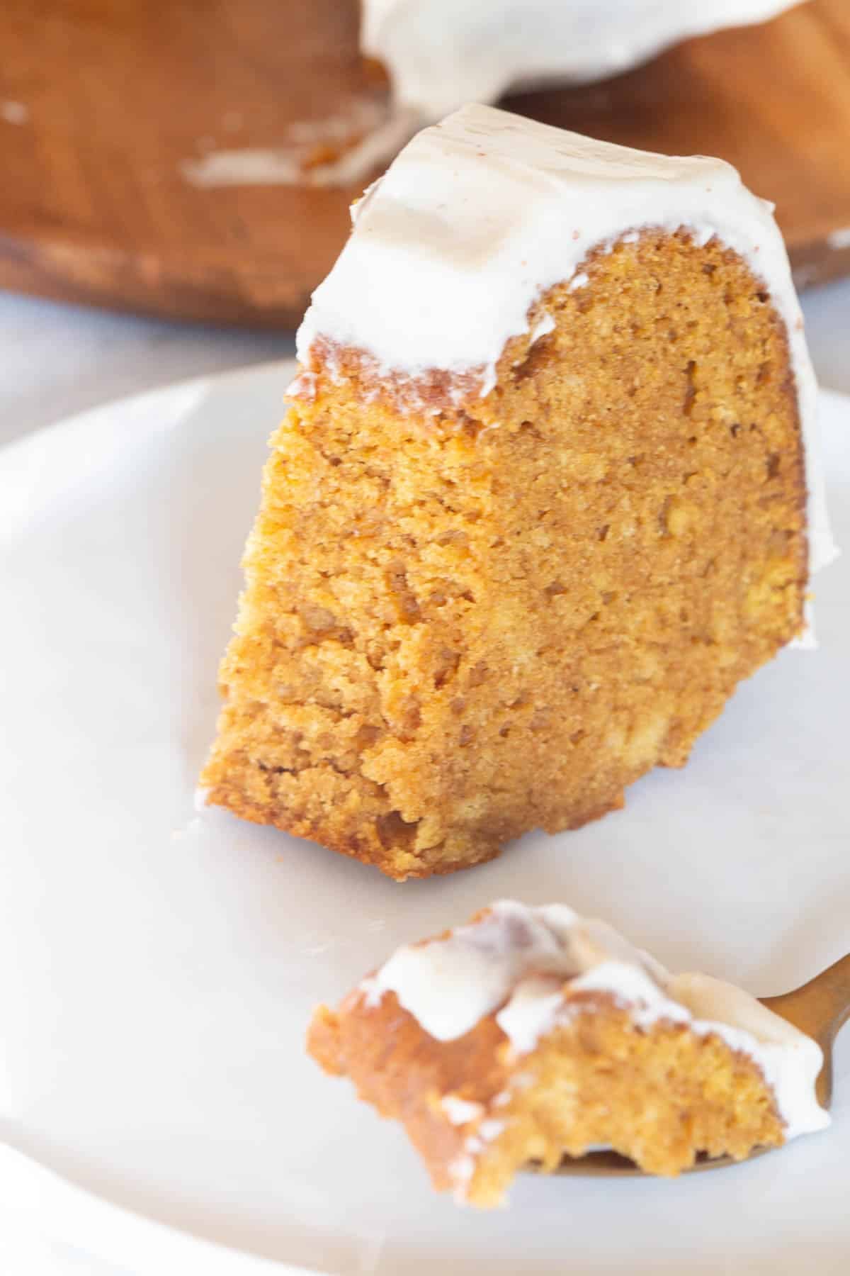 A slice of Pumpkin Bundt Cake with Cream Cheese Frosting with a forkful taken out of it, sitting in front of the slice.