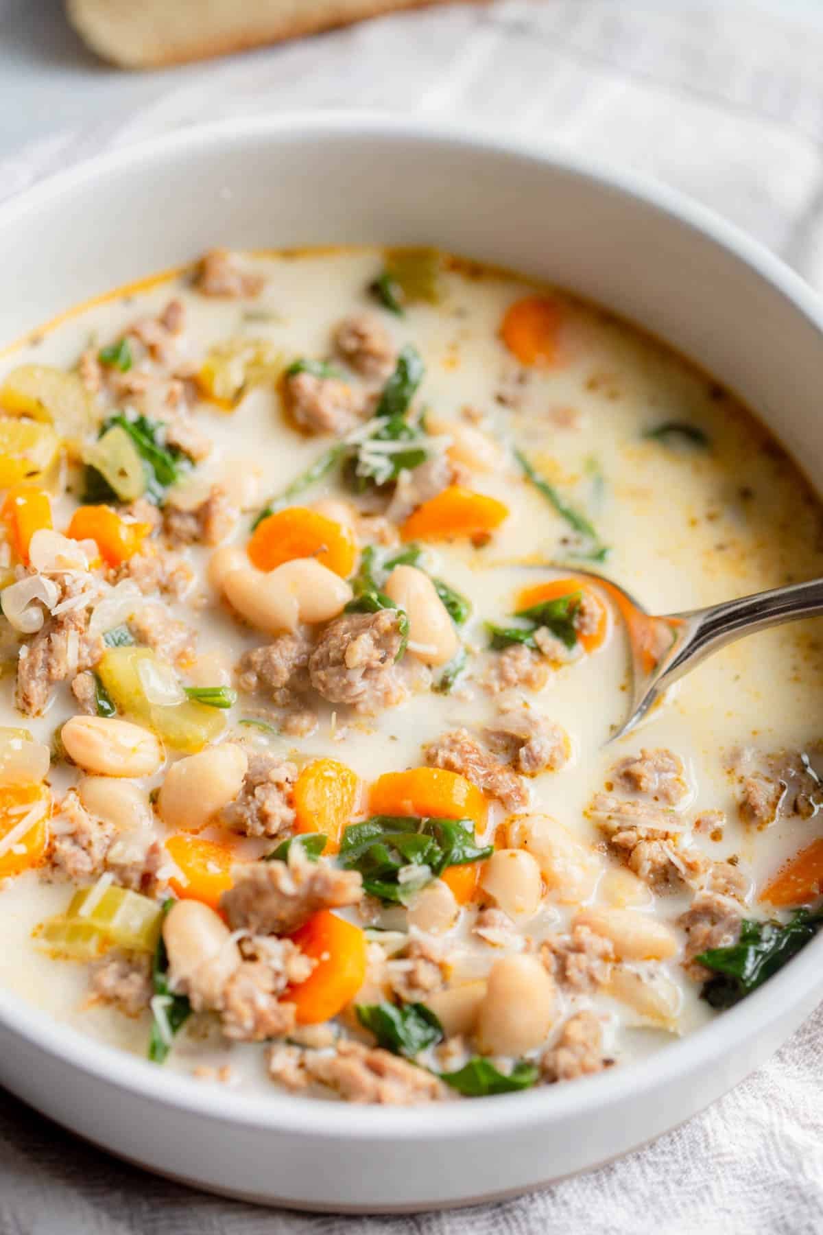 Slow Cooker Sausage and White Bean Soup in a cream colored bowl with a silver spoon resting in it.