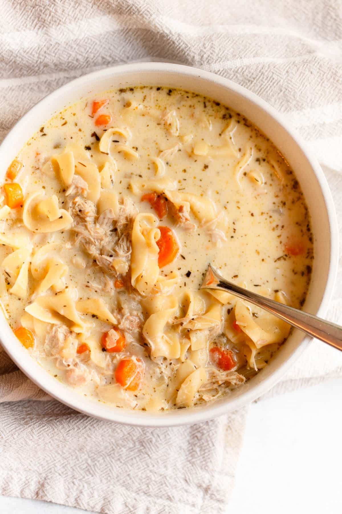 Crock Pot Creamy Chicken Noodle Soup in a white bowl with a silver spoon in it and a tan colored napkin underneath the bowl.