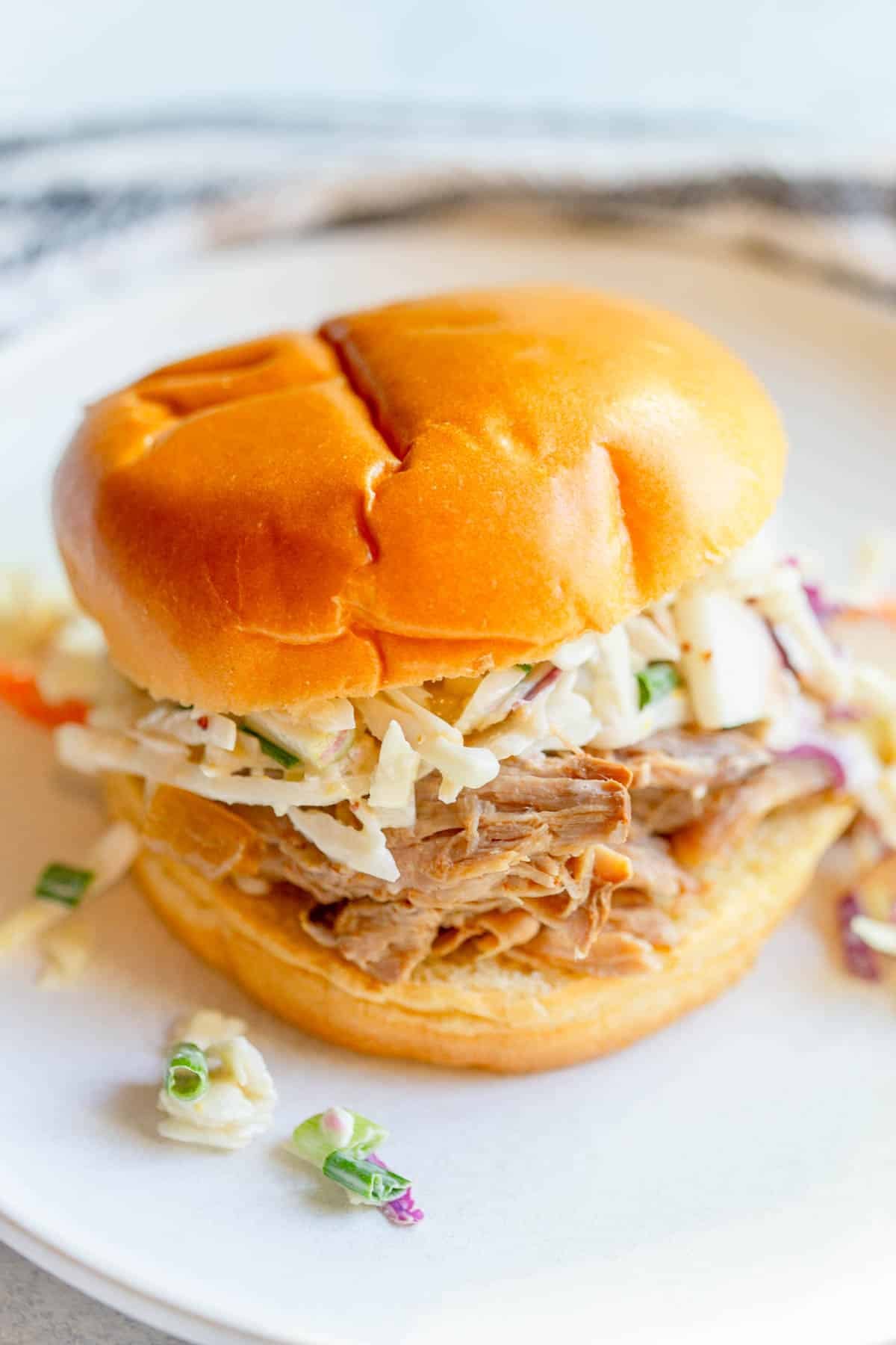 Slow Cooker Apple Cider Pulled Pork on a bun topped with apple cabbage slaw on a white plate.