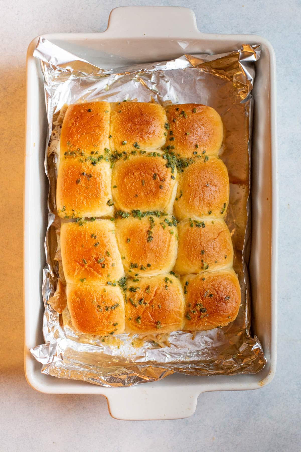 Slow Cooker French Onion Chicken Sliders in a white baking dish lined with foil.