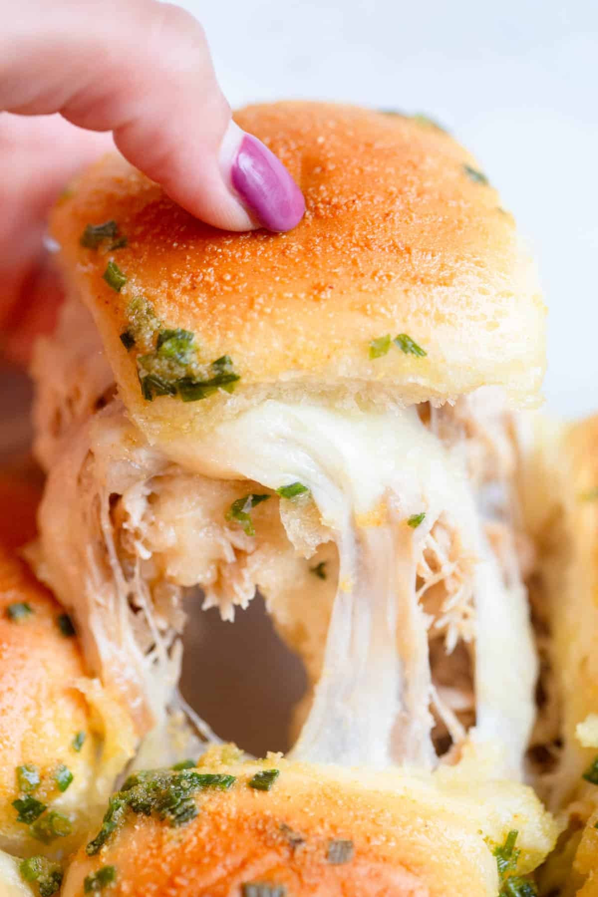 Slow Cooker French Onion Chicken Slider being pulled from another one with a melted cheese pull.