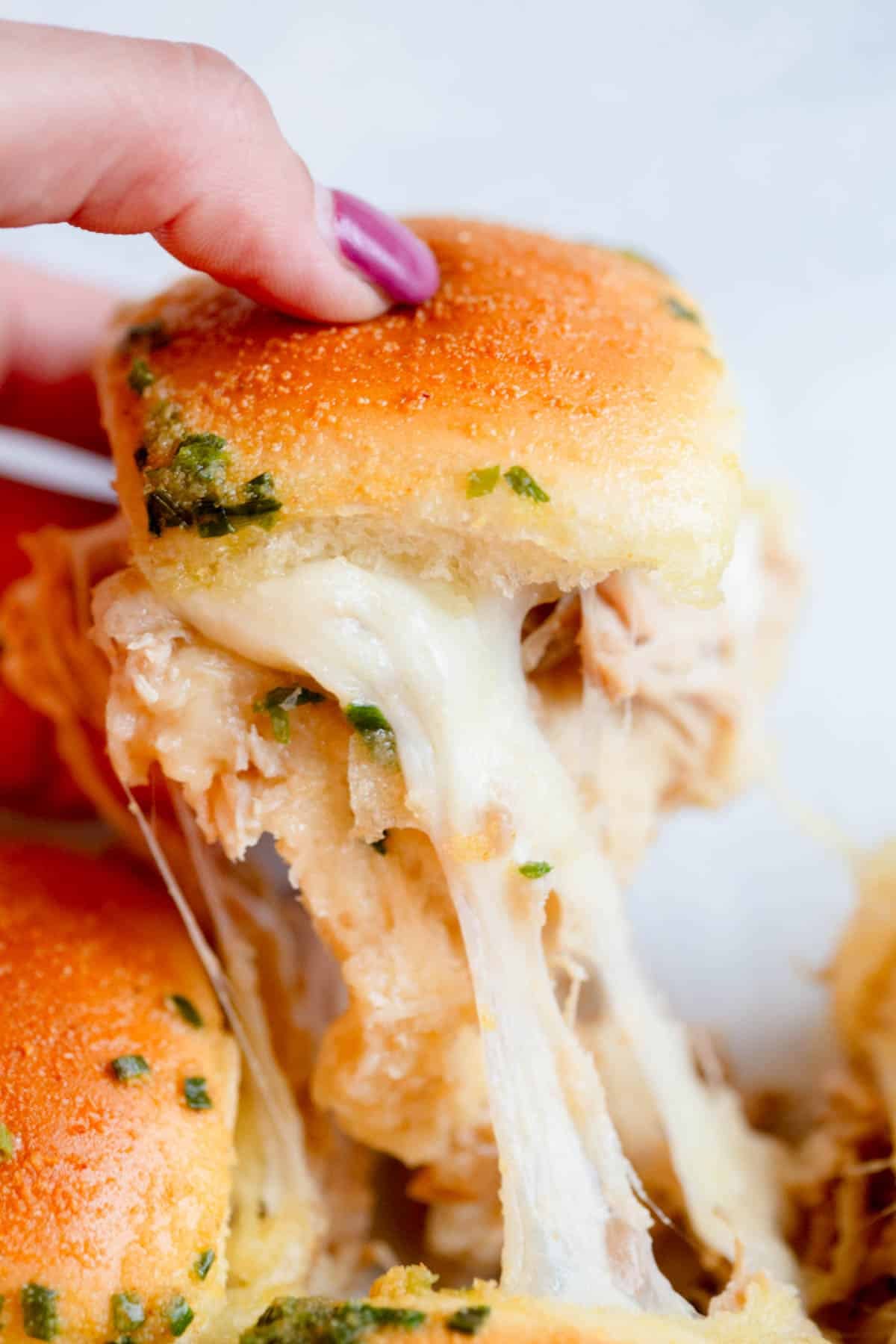 Slow Cooker French Onion Chicken Slider being pulled from another one with melted cheese between them.