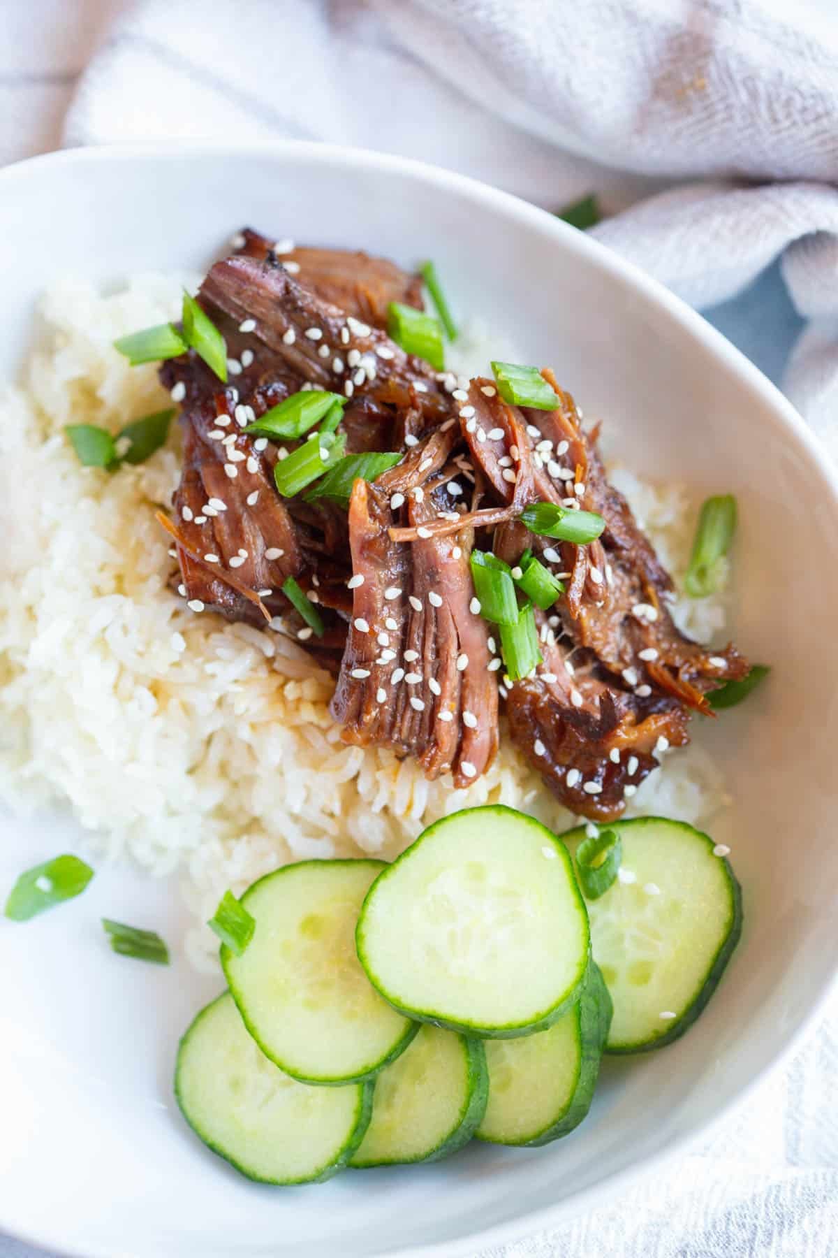 Slow Cooker Japanese BBQ Beef on top of white rice in a shallow bowl topped with sesame seeds and green onions.