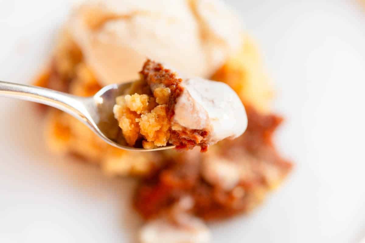 Slow Cooker Pumpkin Dump Cake with a scoop of vanilla ice cream on top on a white plate.