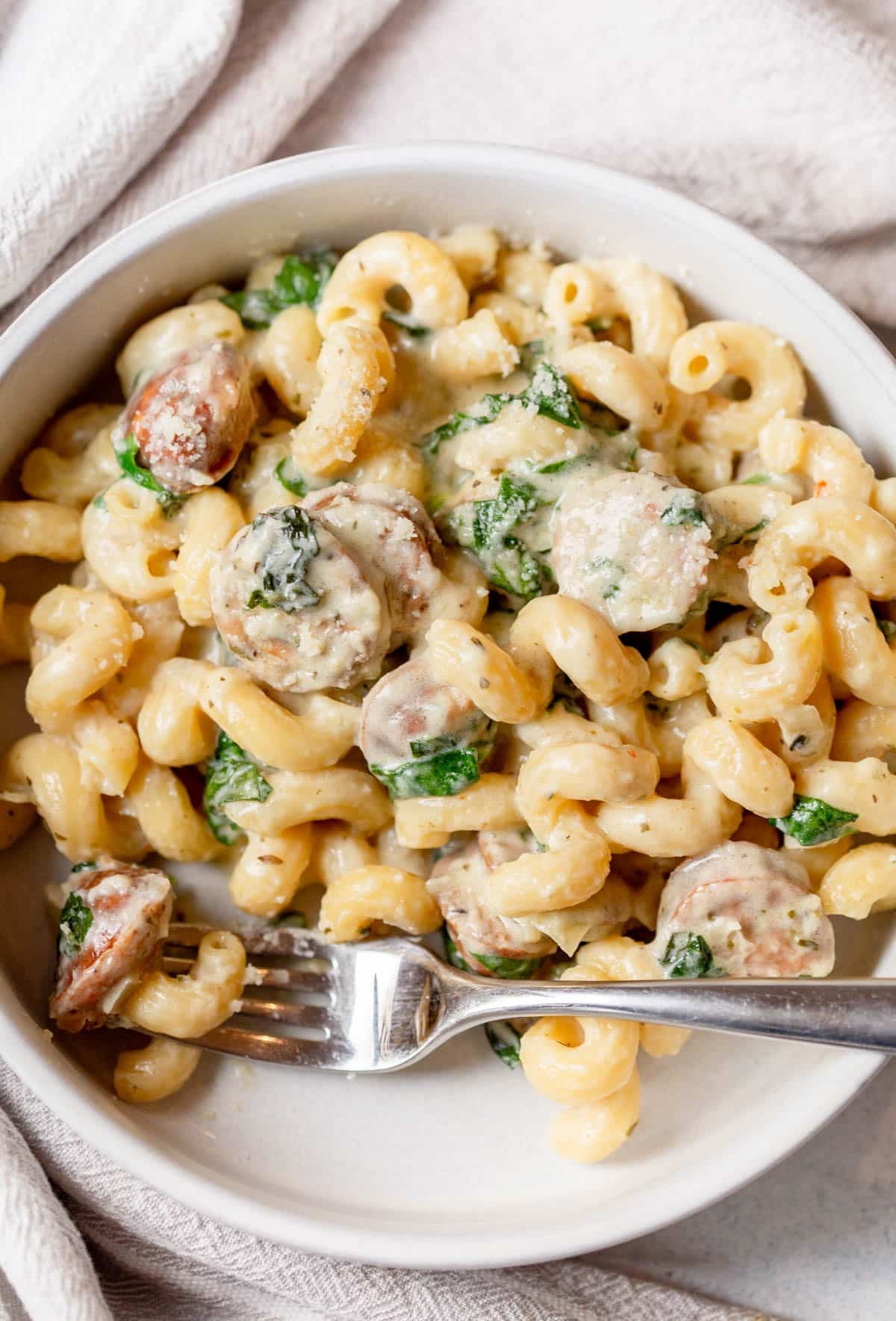 Slow Cooker Sausage Boursin Pasta in a shallow cream colored bowl wiht a fork resting in it.